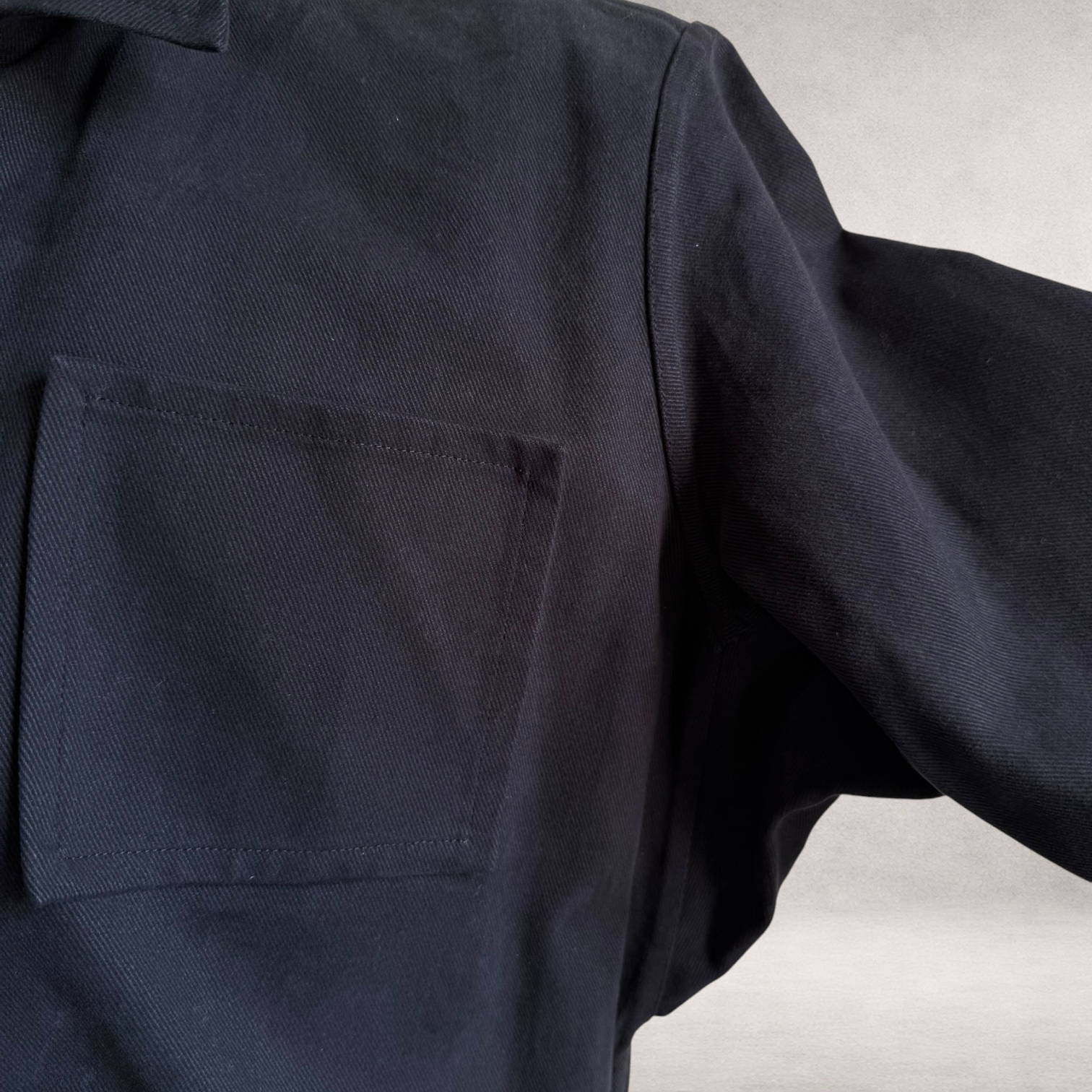 Detail view of the PINTO HERVIA Frame Jacket in black cotton drill showing patch pocket and Aries underarm construction.
