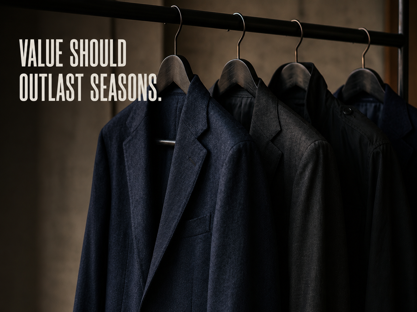 Dark navy and charcoal tailored menswear garments hanging on a rail with overlay text reading “VALUE SHOULD OUTLAST SEASONS.”