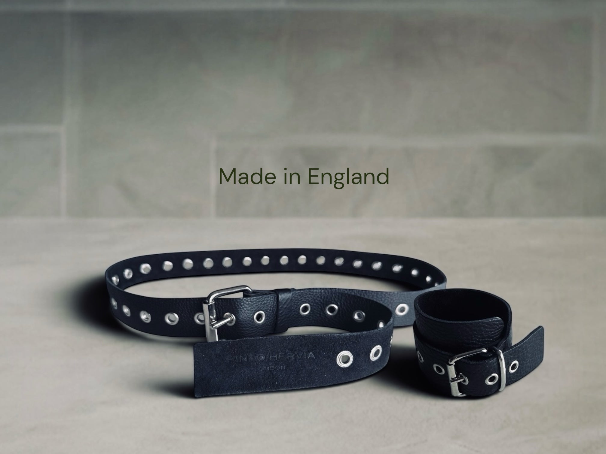 Pinto Hervia accessories collection hero image featuring black leather belt and cuff on stone surface, made in England.