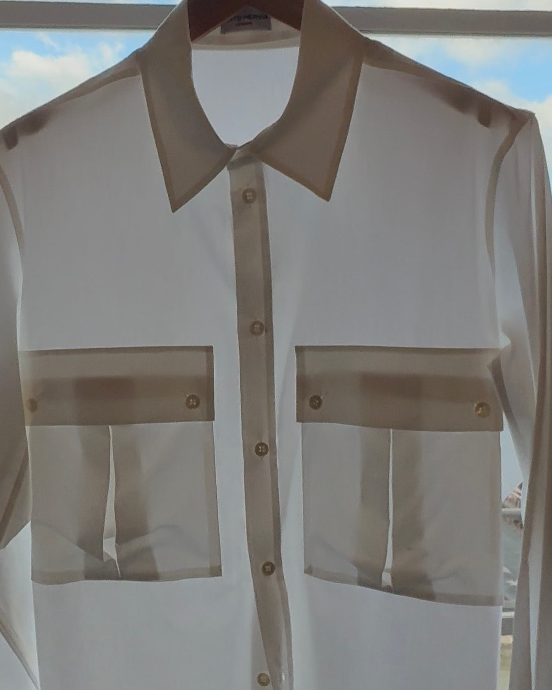 White cotton poplin shirt with contrast collar and chest pockets, hanging on a rail