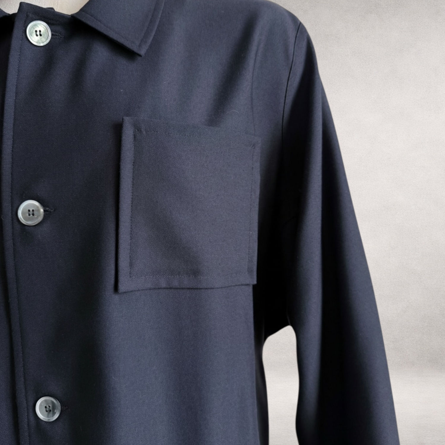 Detail view of the PINTO HERVIA Frame Jacket in black wool showing architectural patch pocket and mother-of-pearl buttons