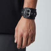 Black leather cuff bracelet worn on wrist with wrap construction and metal hardware
